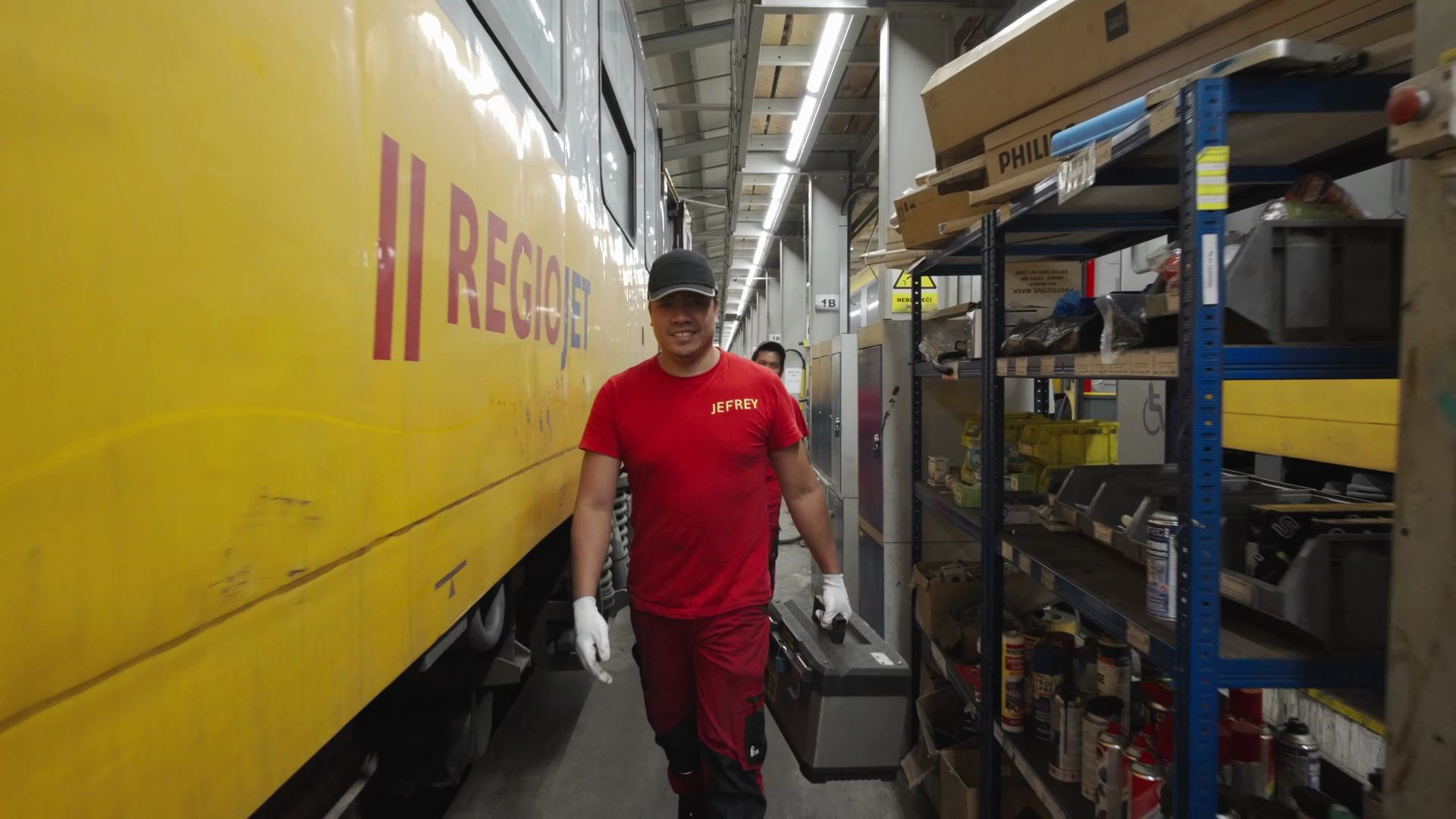 A worker carrying his toolbox along a yellow RegioJet train in the depot