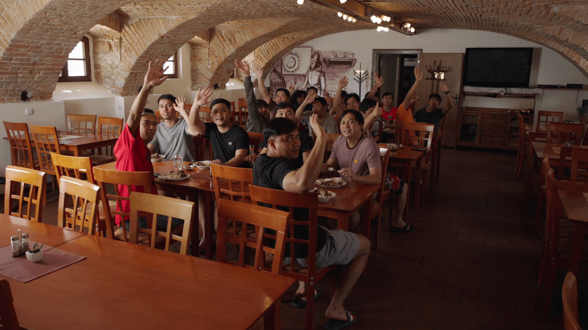 Colleagues at tables in the vaulted dining hall, hands in the air